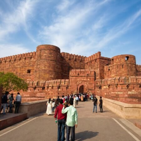 Front view of the historic Agra Fort main entrance with its massive red sandstone walls, circular bastions, and visitors walking towards the gateway in Agra, Uttar Pradesh.