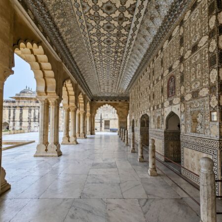 Ornate Sheesh Mahal corridor inside Amber Fort in Jaipur, Rajasthan, featuring intricate mirror work, carved arches, marble flooring, and traditional Rajput architecture.