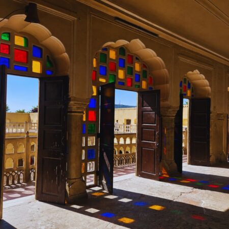 Arched corridor with colorful stained glass windows inside Amber Fort in Jaipur, Rajasthan, featuring traditional Rajput architecture and sunlight reflecting on the stone floor.