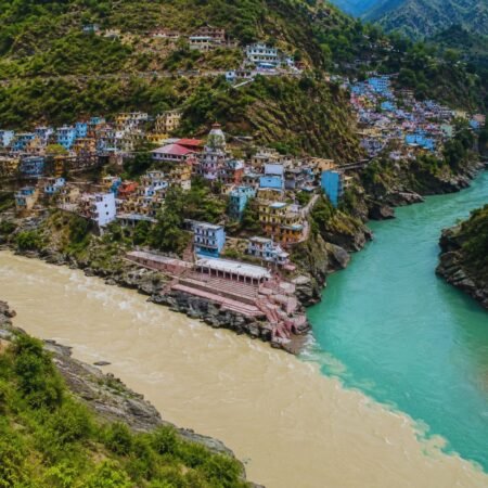 Elevated view of Devprayag Sangam showing the confluence of the Bhagirathi and Alaknanda rivers with the hillside town and surrounding Himalayan landscape in Uttarakhand.