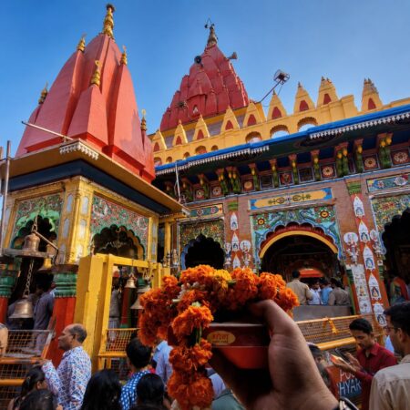 Devotees offering prayers inside the Hanuman Garhi Temple courtyard in Ayodhya, featuring vibrant temple architecture, red shikharas, ornate entrance, and marigold flower offerings.