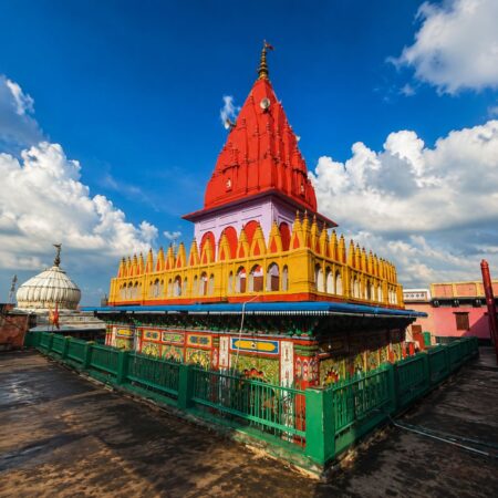 Front view of Hanuman Garhi Temple in Ayodhya featuring its iconic red shikhara, vibrant temple architecture, intricate carvings, and a clear blue sky in the background.