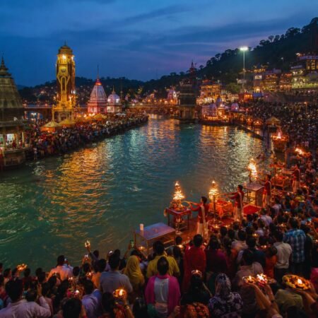 Wide-angle evening view of Har Ki Pauri during the Ganga Aarti in Haridwar, with illuminated ghats, priests performing rituals, and devotees gathered along the River Ganga.
