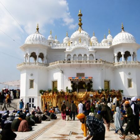 Front view of Takht Sri Keshgarh Sahib in Anandpur Sahib, Punjab, with devotees gathered in the marble courtyard during prayers under a clear blue sky.