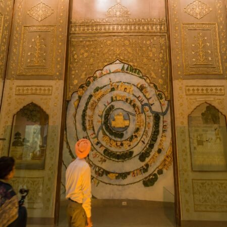 Interior gallery of Virasat-e-Khalsa Museum in Anandpur Sahib featuring an intricate Sikh heritage artwork, ornate golden wall décor, and visitors exploring the museum exhibits.