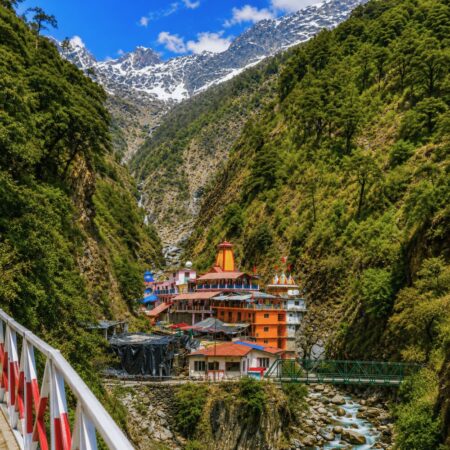 Panoramic view of Yamunotri Temple nestled in the Himalayan valley with snow-capped mountains, river, and lush forests in Uttarakhand.