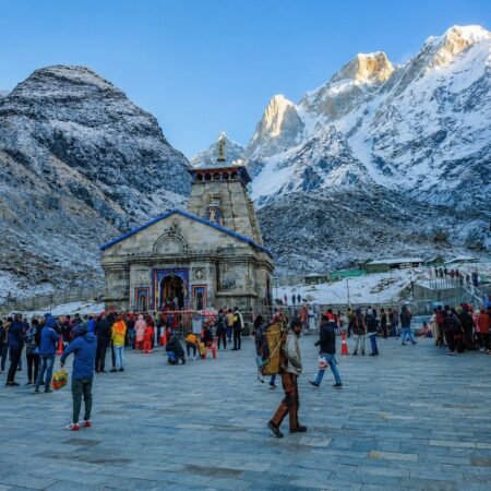 Kedarnath Temple surrounded by snow-covered Himalayan mountains with pilgrims at the temple courtyard