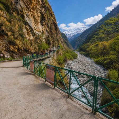 Scenic Yamunotri trek route from Janki Chatti featuring a mountain trail, rocky Yamuna River valley, lush Himalayan landscape, and snow-capped peaks in Uttarakhand.